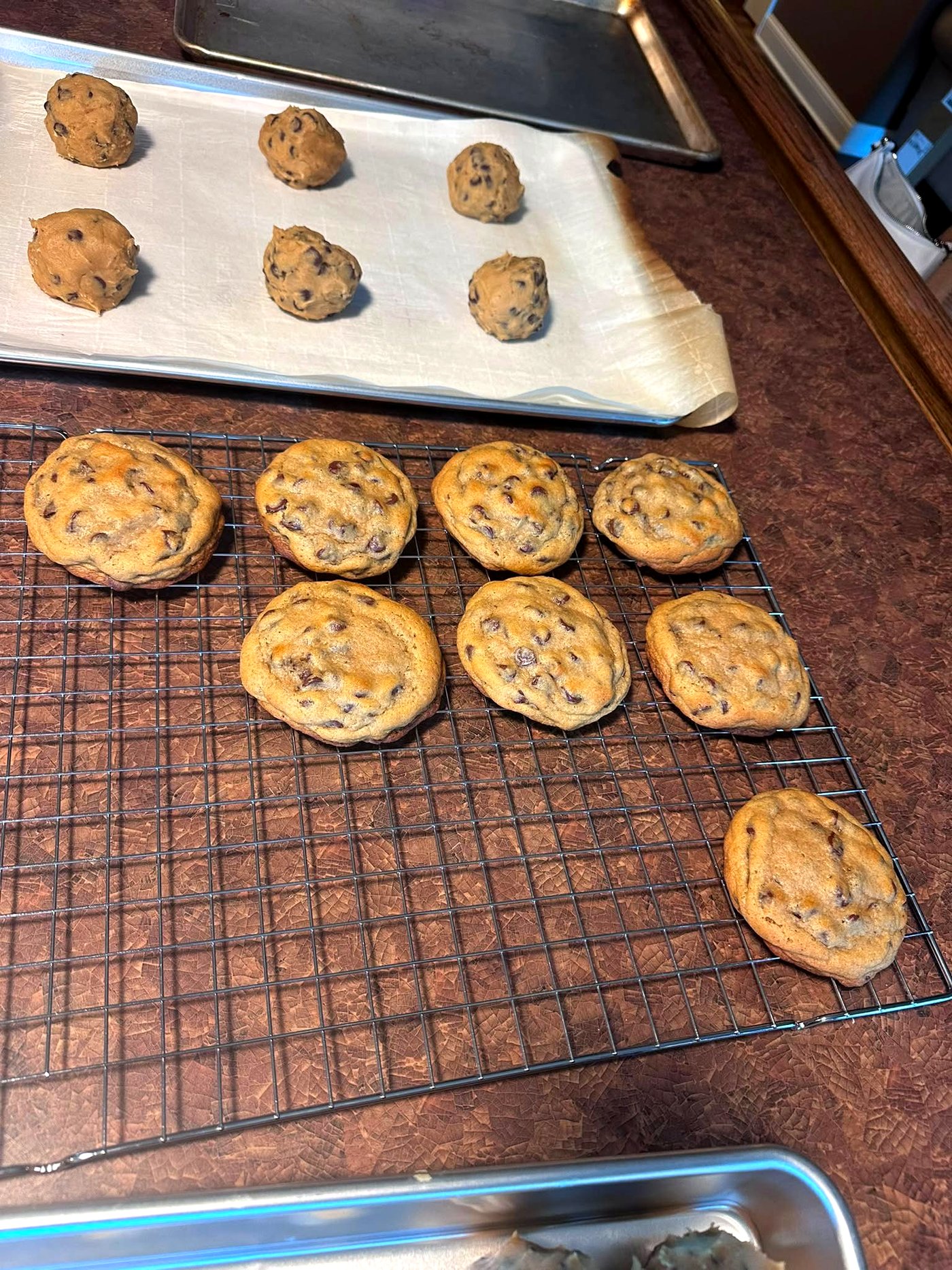 A tray of freshly scooped cookie dough balls alongside a cooling rack of just-baked chocolate chip cookies