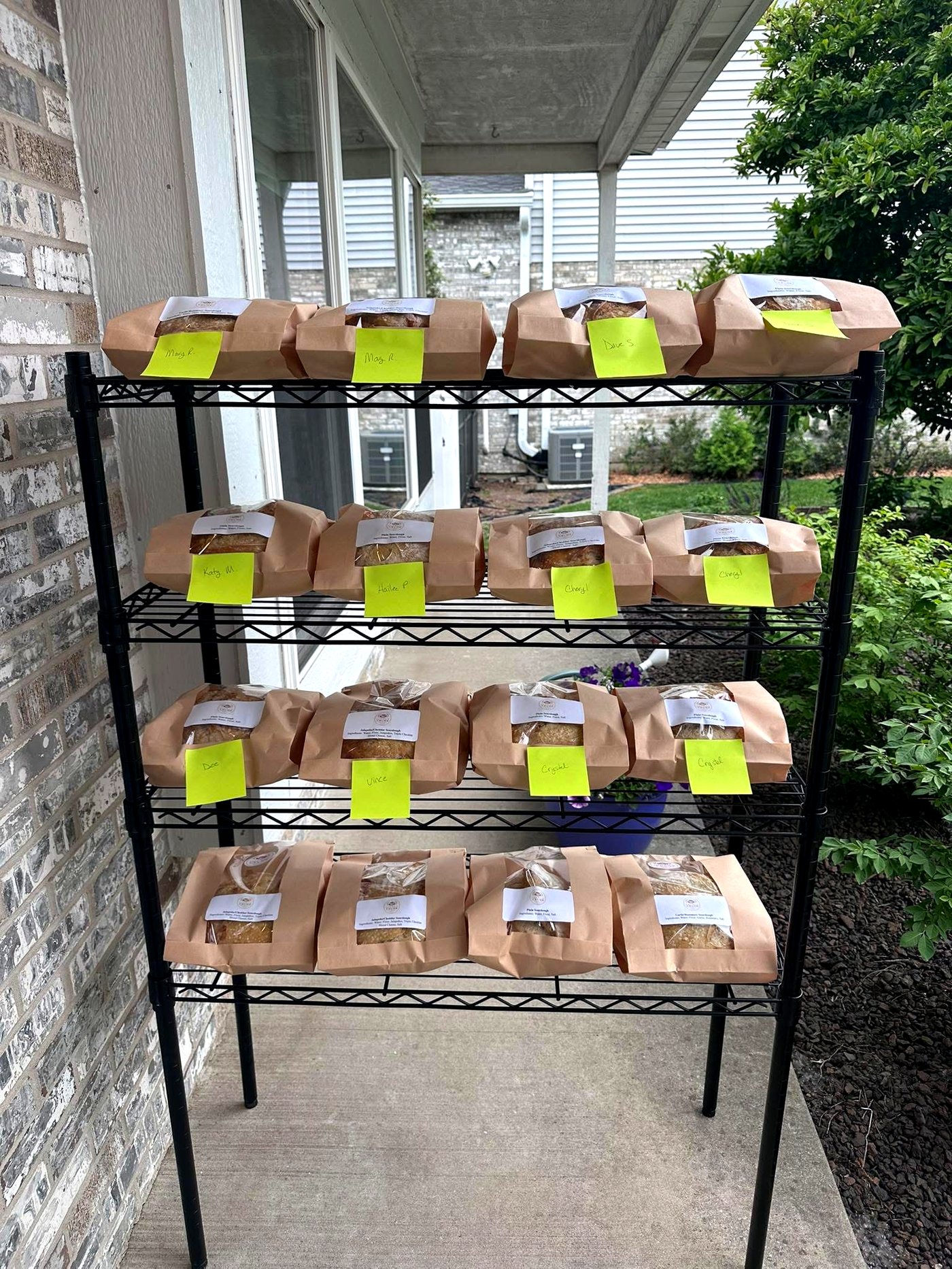 Loaves of sourdough bagged, labeled with customer names, and lined up on the porch rack ready for pickup